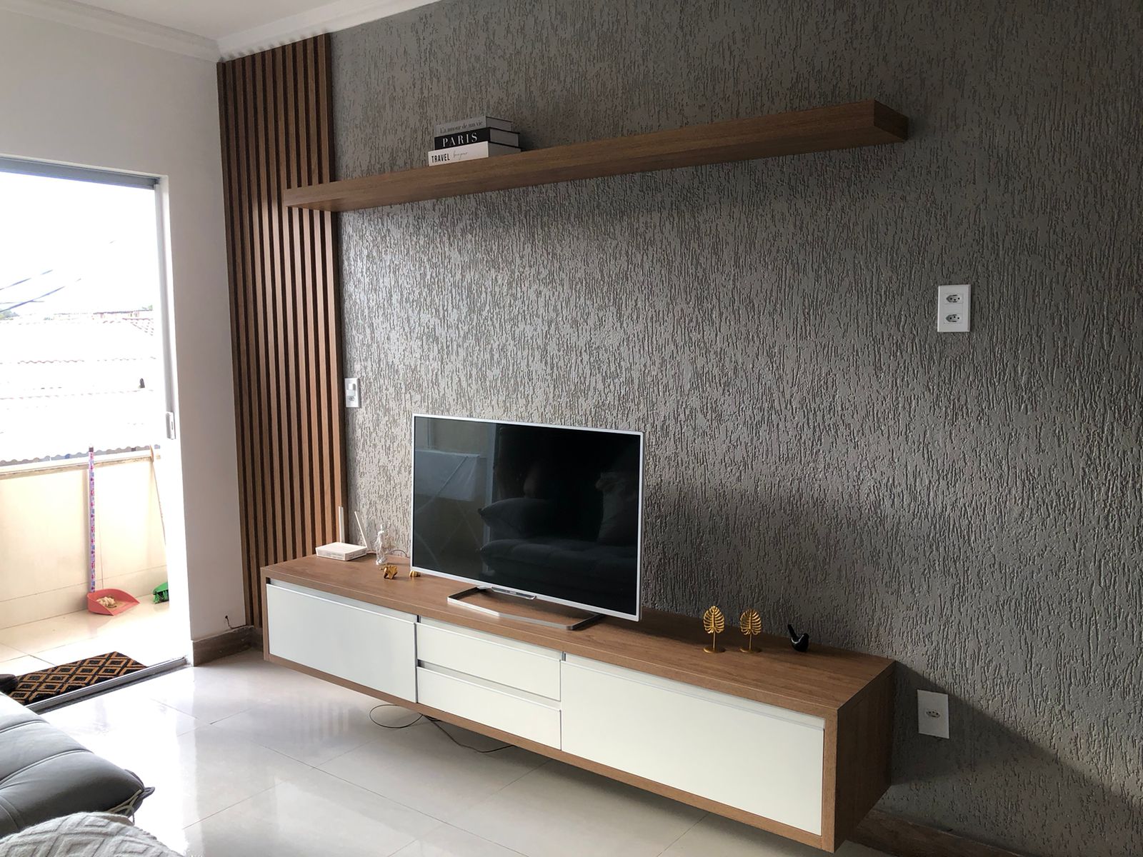 Rack suspenso com gavetas brancas, prateleira decorativa e painel ripado lateral em sala de estar
